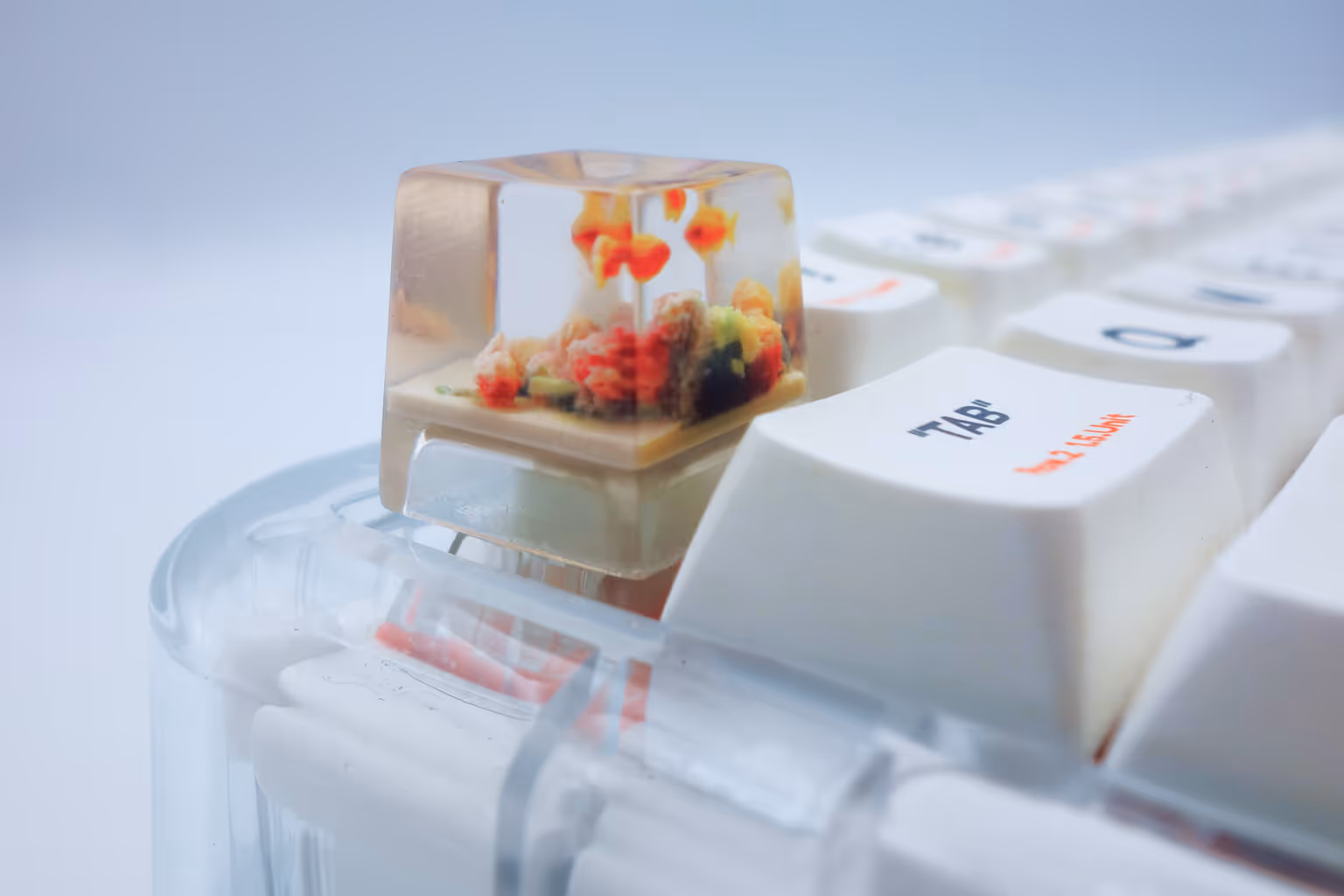 Close-up of a transparent mechanical keyboard keycap with a miniature underwater scene featuring small orange fish inside.
